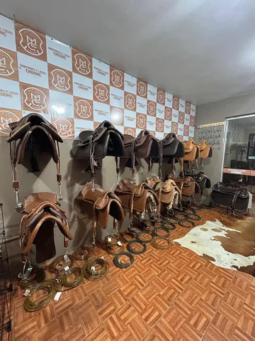Selas expostas na parede com o painel da marca, laços enrolados no chão e um couro de vaca