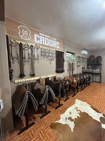 Parede com o letreiro da Cadore, cabeçadas e freios pendurados, badanas e selas em cavaletes