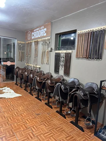 Fileira de selas em cavaletes, com barrigueiras e loros pendurados na parede