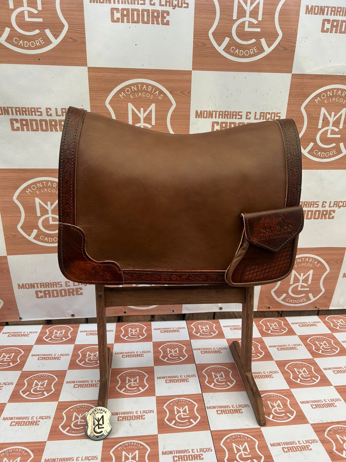 Outra foto da badana de couro marrom com borda trabalhada e bolso personalizado, no cavalete