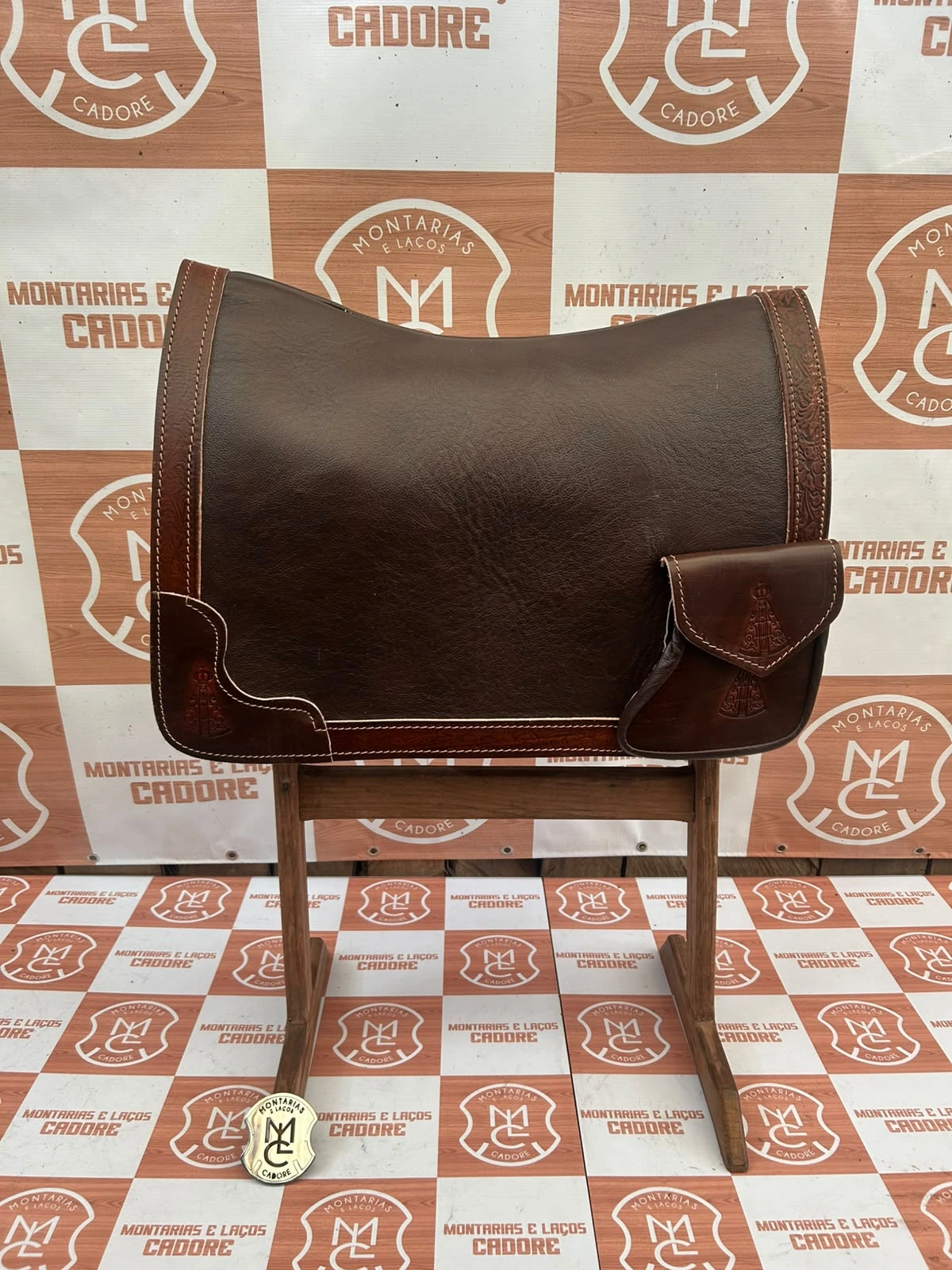 Badana de couro cor café com borda trabalhada e bolso personalizado, sobre cavalete na loja