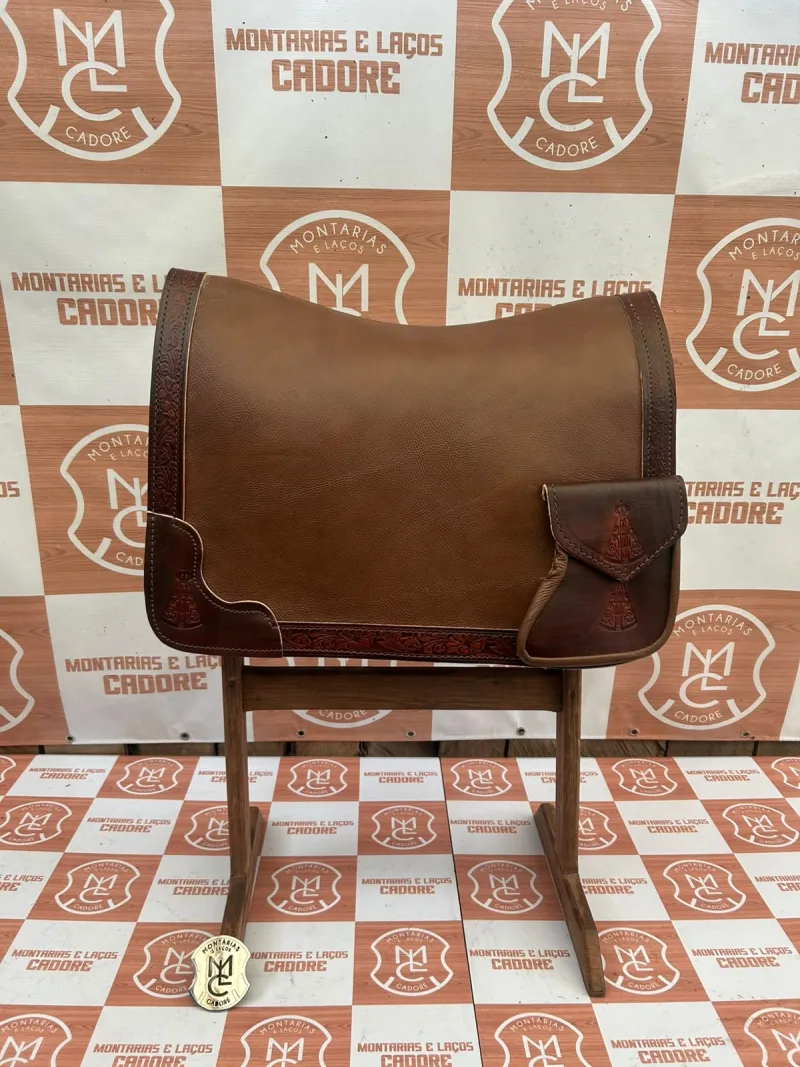 Badana de couro marrom com borda trabalhada e bolso personalizado, sobre cavalete na loja