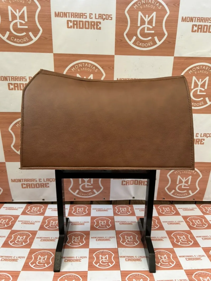 Carona de couro caramelo com costura na borda, apoiada num cavalete