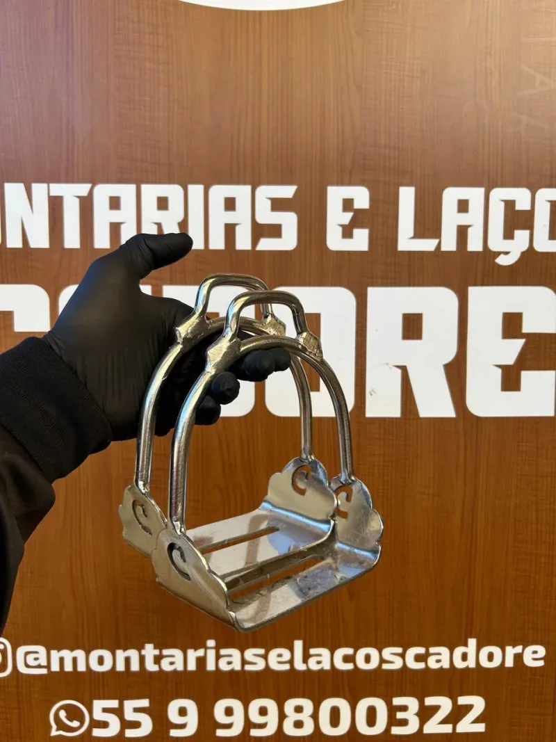 Estribo de inox liso de base larga, segurado com luva preta em frente ao painel da loja