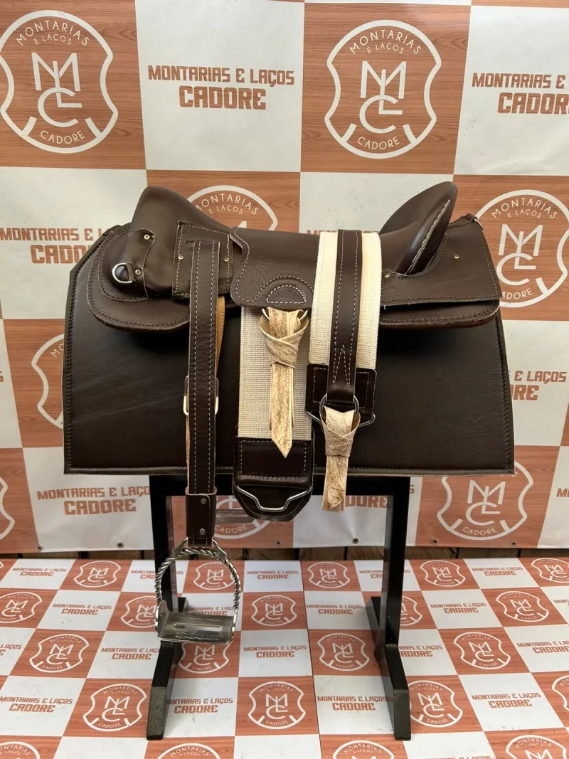 Kit de sela marrom escuro modelo ginete visto de lado, com estribo torcido