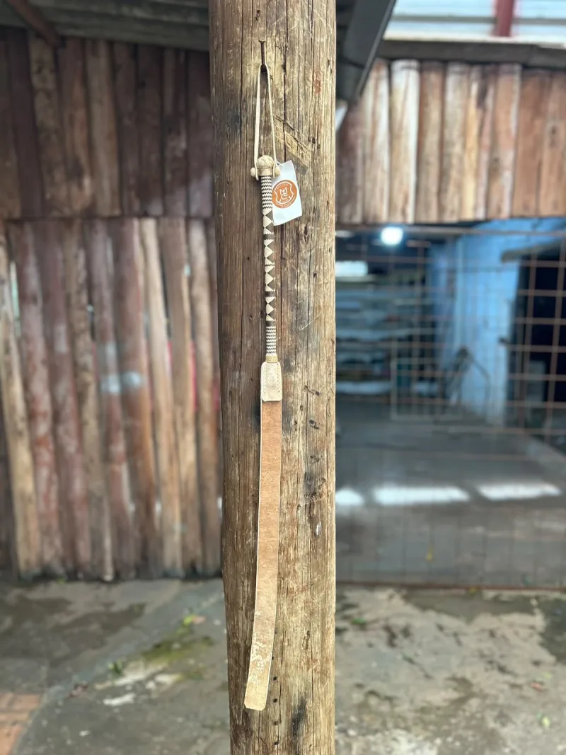 Mango tramado uruguaio inteiro, com cabo trançado em marrom e cru e pala de couro, pendurado num palanque